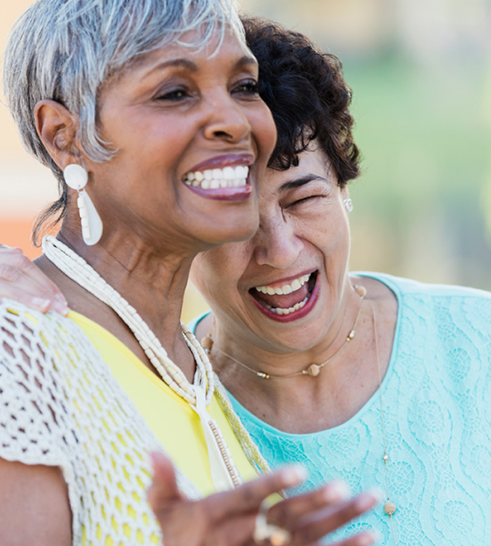 Two senior woman laughing and hugging each other