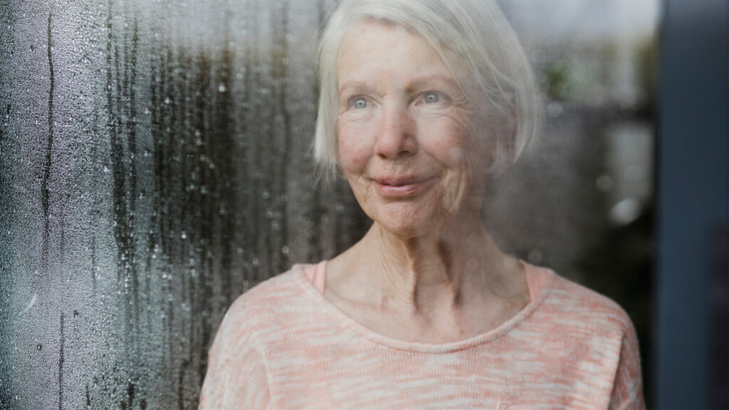 Senior woman looking outside by the window sill during a rainy day