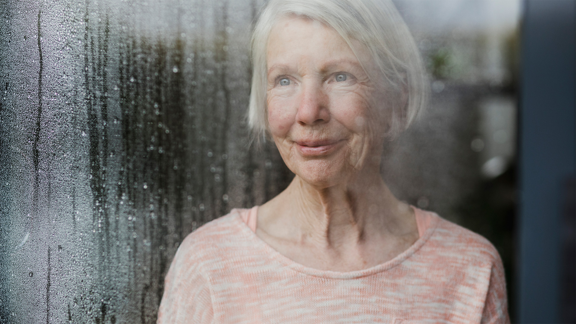 Senior woman looking outside by the window sill during a rainy day