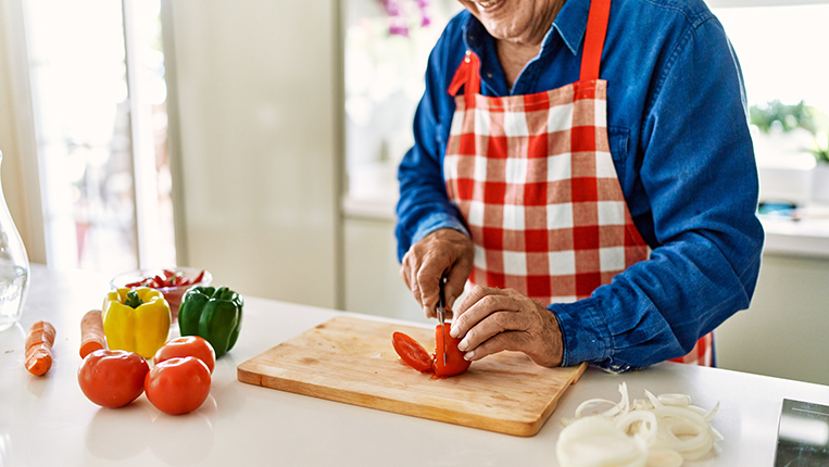 Senior man smiling confident cutting tomato at kitchen