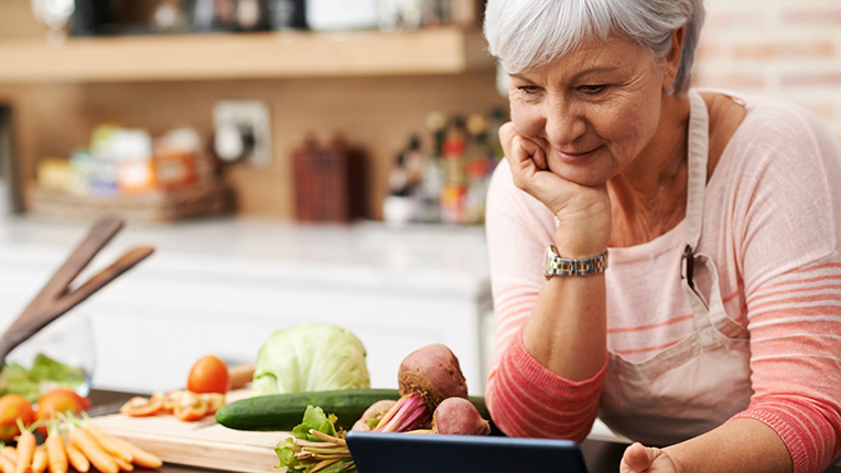 Shot of a woman resting her chin on her hands as she watches a tablet in her kitchen