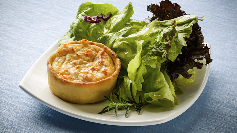 A small quiche with a side salad. On a ceramic white plate on a blue tablecloth