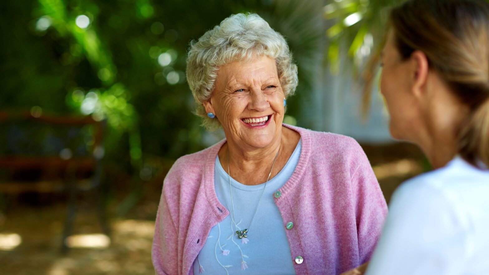 Cheerful senior woman looking at female caretaker in park