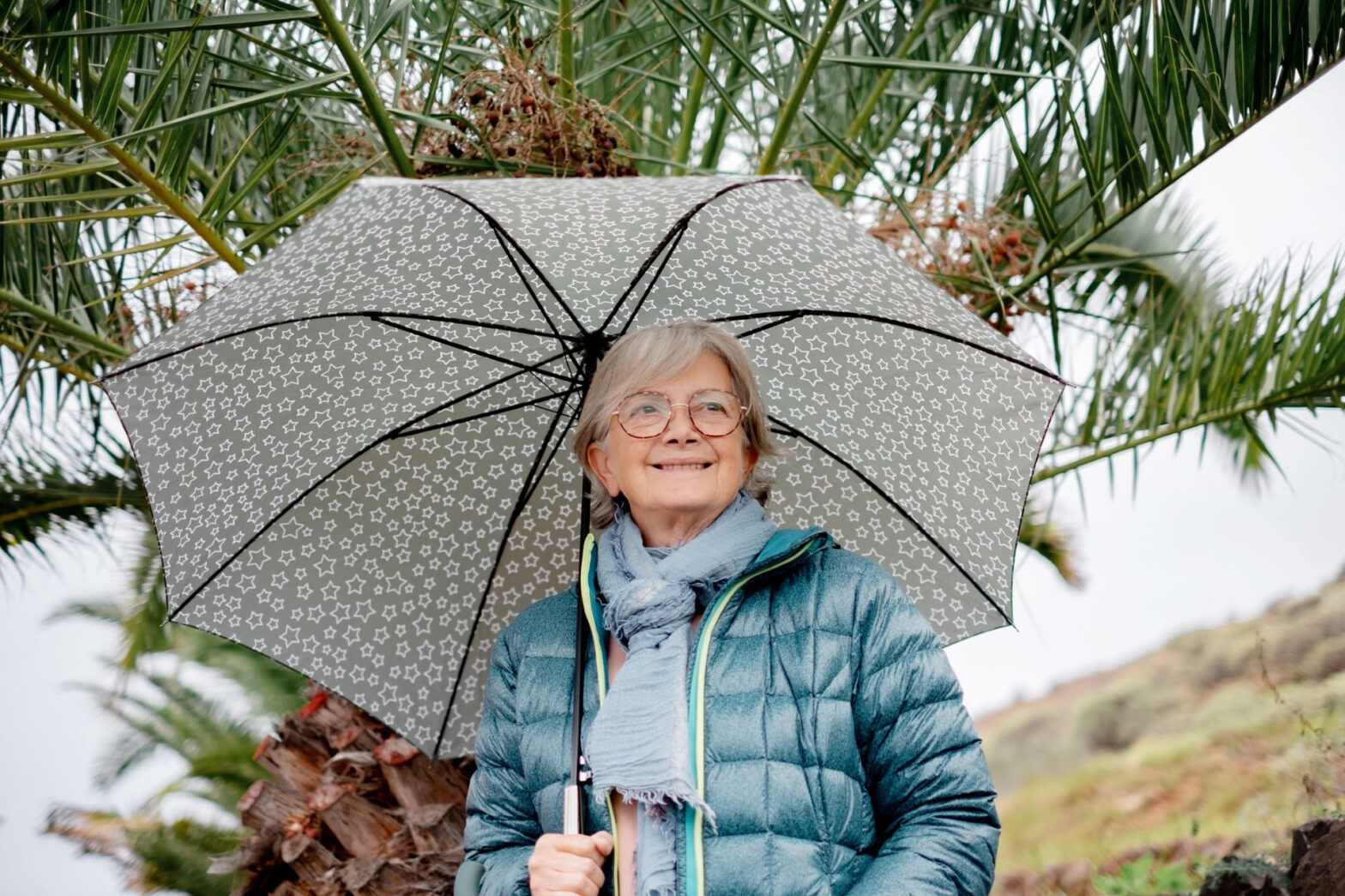 Senior woman holding an umbrella and wearing a thick jacket and scarf during a cold-weather day