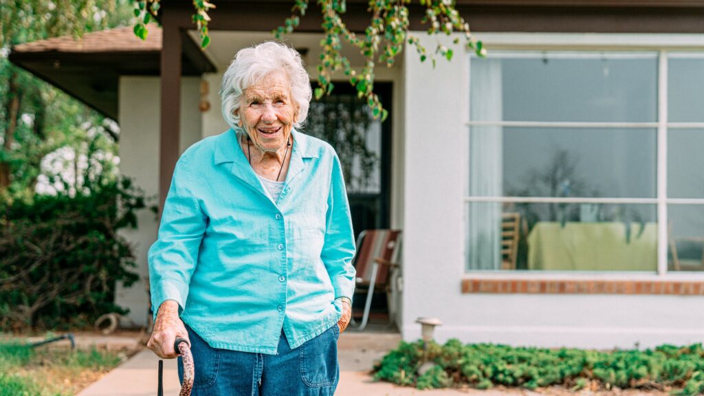 Older woman standing outdoors in front of her home in the summer