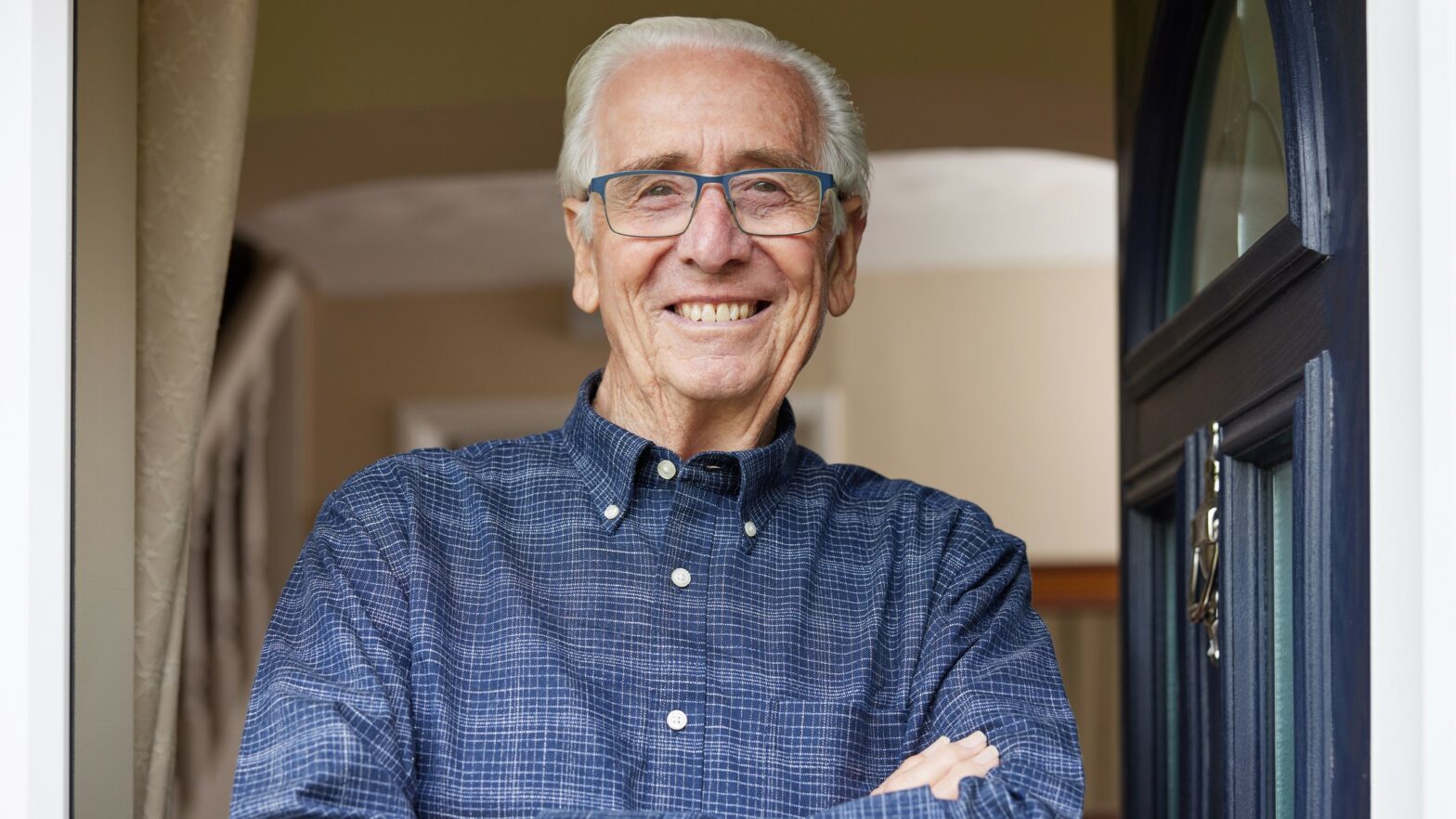 Smiling senior man standing at open front door of house