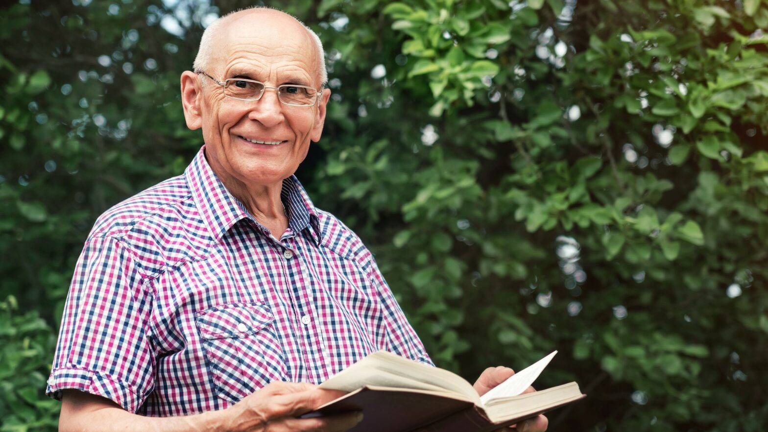 Portrait of happy senior man with book in hands against greenery