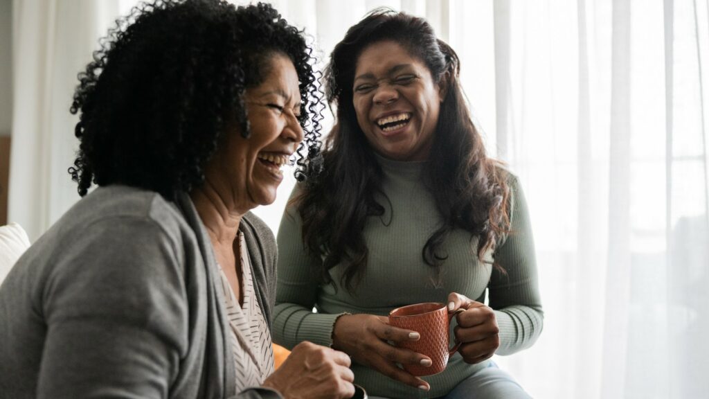 Happy friends or mother and daughter talking and drinking coffee at home