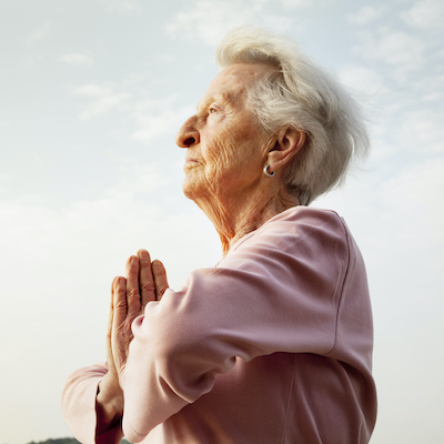 senior woman, 88 years old, active and flexible, practising yoga at a lake at a sunny summer morning, folding hands